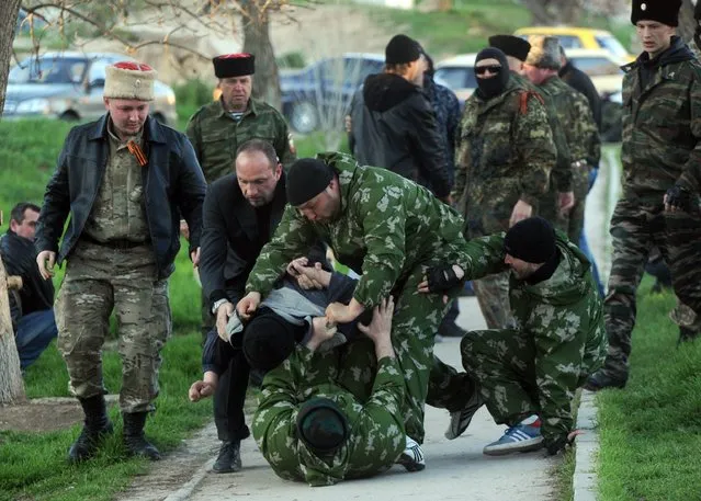Pro-Russian militiamen beat an unidentified man as Russian soldiers stormed a Ukrainian military air base in the small city of Belbek near the Crimean city of Sevastopol on March 22, 2014. Armed forces backed by armoured vehicles broke inside a Ukrainian airbase in Crimea on Saturday, firing automatic weapons into the air. (Photo by Viktor Drachev/AFP Photo)