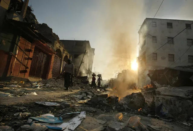 People walk through fire and rubble in the market area in Port-au-Prince, Monday, January 18, 2010. On the streets, people are still dying, pregnant women are giving birth and the injured are showing up in wheelbarrows and on people's backs at hurriedly erected field hospitals after Tuesday's earthquake. (Photo by Gerald Herbert/AP Photo)