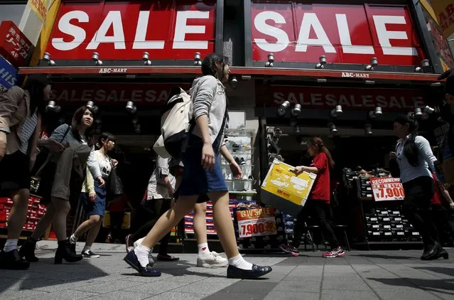 A shop clerk (2nd R) carries a box of shoes under sale signboards at a shoes retail store at a shopping district in Tokyo, Japan, April 28, 2015. (Photo by Yuya Shino/Reuters)