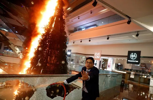 A man reacts as he tries to extinguish a burning Christmas tree at Festival Walk mall in Kowloon Tong, Hong Kong, November 12, 2019. Anti-government protesters smashed windows and set fires in the mall on Tuesday, including to a big Christmas tree. (Photo by Thomas Peter/Reuters)
