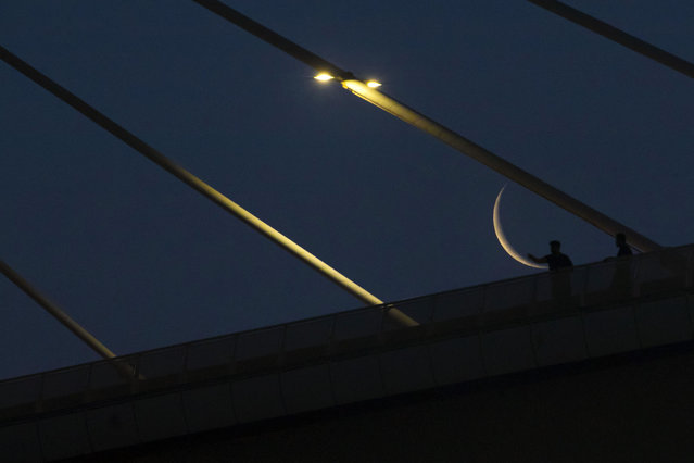 The waning crescent moon, near the end of the Muslim holy month of Ramadan, is pictured behind the Mohammad Baqir al-Sadr bridge in Iraq's southern city of Basra early on April 28, 2022. (Photo by Hussein Faleh/AFP Photo)