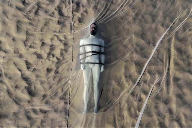 Seen from above, a life size mannequin representing bricklayer Amarildo de Souza, a resident of the Rocinha favela who disappeared 10 years ago, lays under netting on Copacabana beach during a protest against his disappearance in Rio de Janeiro, Brazil, Thursday, July 13, 2023. (Photo by Bruna Prado/AP Photo)