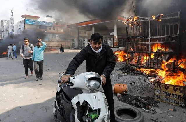 A man pushes his damaged scooter past a burning petrol pump during a clash between people supporting a new citizenship law and those opposing it, in New Delhi India, February 24, 2020. (Photo by Danish Siddiqui/Reuters)