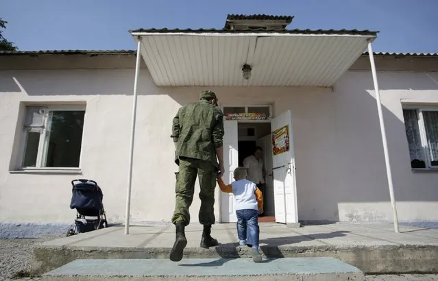 A man wearing a camouflage uniform walks with a child as they enter a school on the start of the new school year in Donetsk, Ukraine, September 1, 2015. (Photo by Alexander Ermochenko/Reuters)