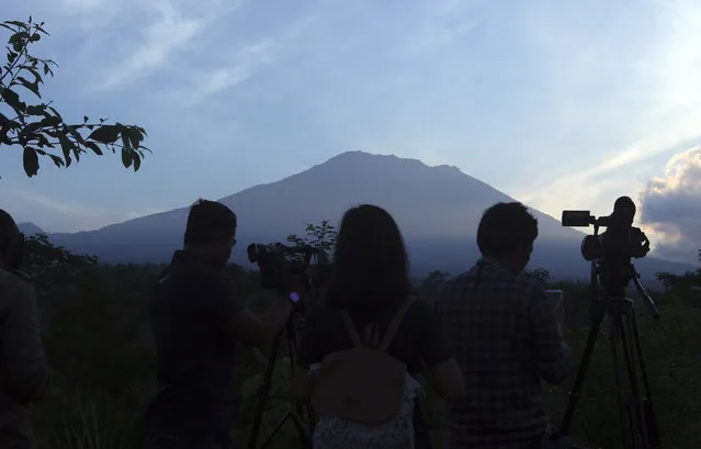 Journalists watch Mount Agung from an observation point which is about 12 kilometer (7.4 miles) away from the volcano in Karangasem, Bali, Indonesia, Thursday, September 28, 2017. The exodus from the menacing volcano on the Indonesian tourist island is nearing 100,000 people, a disaster official said Wednesday, as hundreds of tremors from the mountain are recorded daily. (Photo by Firdia Lisnawati/AP Photo)