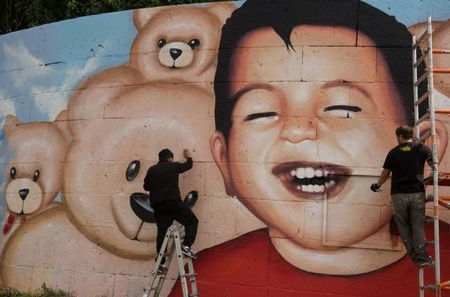 Graffiti artists Oguz Sen, left, and Justus Becker put the finishing touches to a new mural of the drowned Syrian refugee Aylan Kurdi, at Osthafen in Frankfurt am Main, Germany on July 4, 2016. After the previous picture was daubed with slogans, the new image shows a living, laughing Aylan surrounded by teddy bears. (Photo by Boris Roessler/DPA via ZUMA Press)