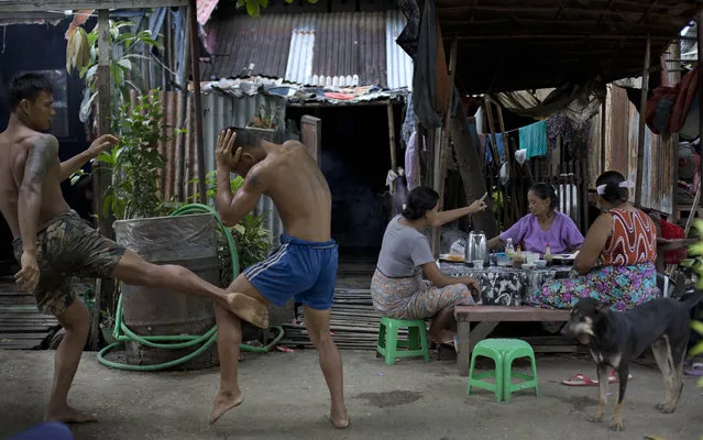 In this Wednesday, July 15, 2015, photo, a member of the White New Blood lethwei fighters club, a Myanmar traditional martial-arts club which practices a rough form of kickboxing,  practice in their gym on a street as customers eat a meal at a roadside noodles shop in Oakalarpa, north of Yangon, Myanmar. (Photo by Gemunu Amarasinghe/AP Photo)