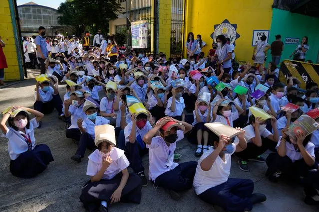 Students place books on their heads for protection during an earthquake drill at an elementary school in Metro Manila, Philippines on Thursday September 8, 2022. The Philippines conducted its third quarter nationwide earthquake drill as part of efforts to make the public aware of protocols and response during a disaster. (Photo by Aaron Favila/AP Photo)