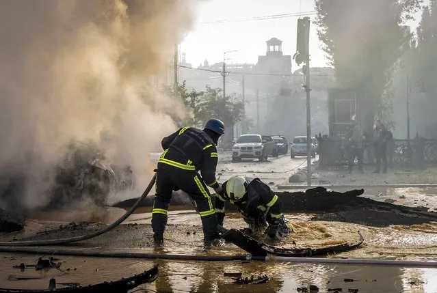 A firefighter helps his colleague to escape from a crater as they extinguish smoke from a burned car after a Russian attack in Kyiv, Ukraine, Monday, October 10, 2022. Russia unleashed a lethal barrage of strikes against multiple Ukrainian cities Monday, smashing civilian targets including downtown Kyiv where at least six people were killed amid burnt-out cars and shattered buildings. The onslaught brought back into focus the grim reality of war after months of easing tensions in the capital. (Photo by Roman Hrytsyna/AP Photo)