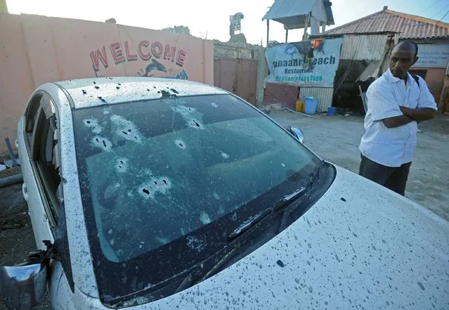 A man stands next to a car with impacts of bullets next to the beach restaurant in the capital Mogadishu on August 26, 2016 one day after an attack by alleged Al-Qaeda-linked Shebab rebels killed nine people including the assailants, according to Mogadishu city spokesman Abdifatah Halane. Al-Qaeda-linked Shebab rebels attacked a beachfront restaurant in the Somali capital Mogadishu on August 25, setting off a car bomb before exchanging fire with security forces, an AFP correspondent said. The Al-Qaeda-linked Shabaab group claimed responsibility for the attack through the website of their Andalus radio station. (Photo by Mohamed Abdiwahab/AFP Photo)