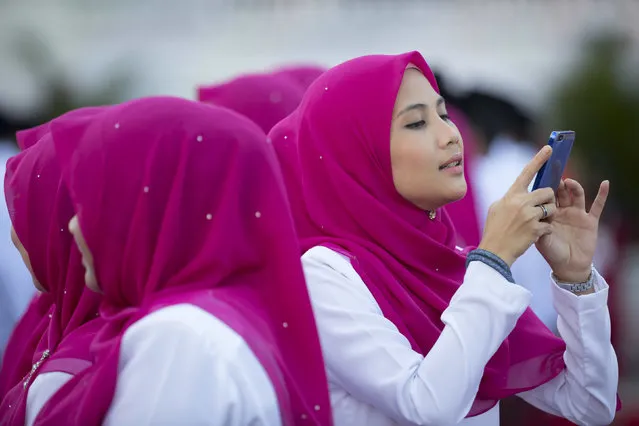 A member of United Malays National Organisation (UMNO) party takes a picture with her cellphone before the opening ceremony of the party's general assembly in Kuala Lumpur, Malaysia, Thursday, December 7, 2017. Malaysian Prime Minister Najib Razak is expected to rally for unity in the three days annual assembly ahead of the general elections which must be held by August 2018. (Photo by Vincent Thian/AP Photo)