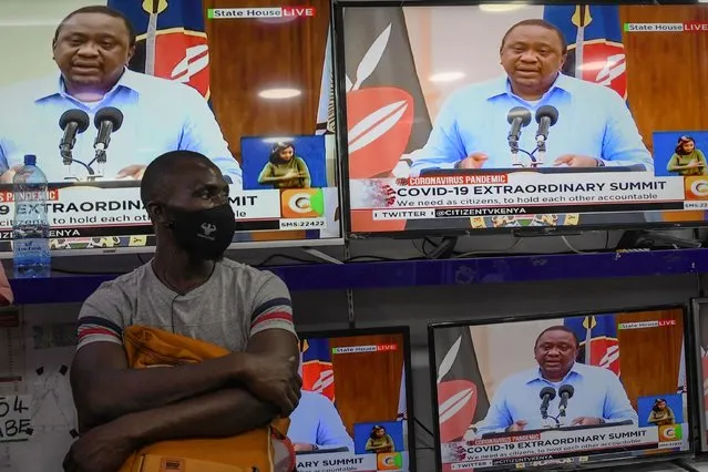 A man wearing a face mask stands inside an electronics shop as Kenya's President Uhuru Kenyatta is seen on television screens while giving an address to the nation on the COVID-19 (novel coronavirus) pandemic, and measures that the government maintain and enforce to curb the disease's spread, on July 27, 2020, in Nairobi. - Kenyan President Uhuru Kenyatta on July 27, banned the sale of alcohol in eateries and restaurants and extended a curfew in a bid to halt a steep rise in coronavirus infections. Kenyatta delivered a stern dressing down to Kenyans for “reckless” behaviour that has seen cases triple in the past month to 17,975, while 285 have died. (Photo by Simon Maina/AFP Photo)