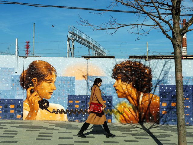 A woman walks past a fence with a mural on the street in Moscow, Russia on April 14, 2025. (Photo by Evgenia Novozhenina/Reuters)