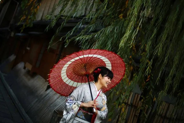 A woman, dressed in a traditional Japanese kimono, poses for tourists in Kyoto, western Japan November 19, 2014. (Photo by Thomas Peter/Reuters)
