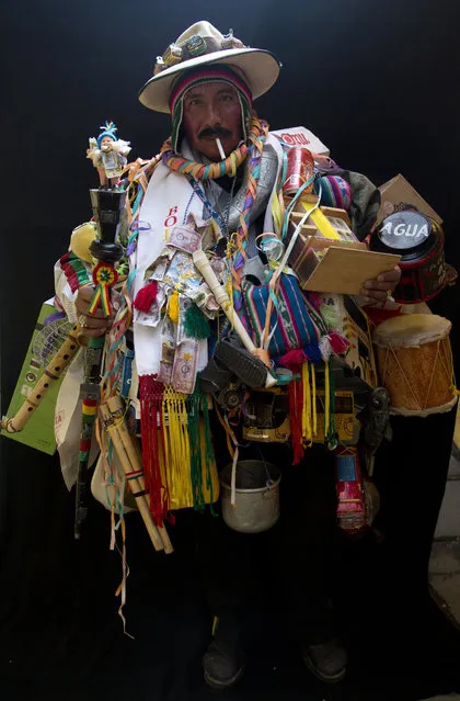 In this February 6, 2018 photo, Juan Ricaldi, dressed as “Ekeko”, the god of prosperity, is covered in objects including instruments as he holds a cigarette in his mouth during a portrait session on the sidelines of the annual Alasita Fair in La Paz, Bolivia. “For me, the Ekeko hasn't made me rich but allows me to live”, said the 59-year-old artisan. “I can say that the Ekeko has made my dreams come true, has never left me and will be with me forever”, he said. Ricaldi won this year's Ekeko competition. (Photo by Juan Karita/AP Photo)