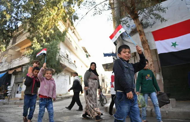 Syrian children wave national flags as they walk in al-Hellok neighbourhood in the northern city of Aleppo, after Syrian army forces replaced the Kurdish People's Protection Units (YPG) which had previously been in control, on February 23, 2018. (Photo by George Ourfalian/AFP Photo)