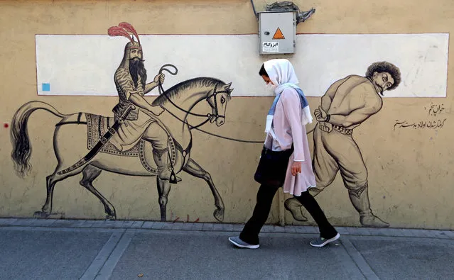 A woman, wearing a protective mask due to the COVID-19 coronavirus pandemic, walks past a graffiti depicting the legendary Persian hero Rustam (or Rostam) riding his horse behind a bound prisoner in Iran's capital Tehran on September 20, 2020. Iran called on the rest of the world to unite against the United States, after Washington unilaterally declared UN sanctions against the Islamic republic were back in force. Washington has said it will “impose consequences” on any country not complying with the sanctions, although the US is one of the only nations that believes they are in force. (Photo by Atta Kenare/AFP Photo)