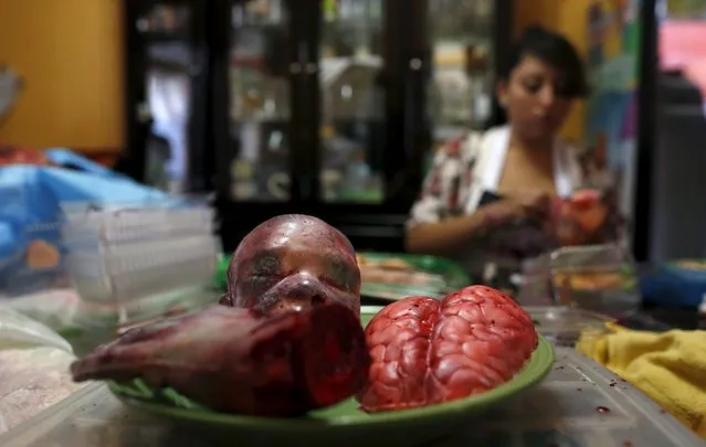 A bloody zombie baby head, brain and a hand made of gummy candy and red jelly are pictured as a woman works (rear) at the Zombie Gourmet homemade candy manufacturer on the outskirts of Mexico City October 30, 2015. (Photo by Carlos Jasso/Reuters)