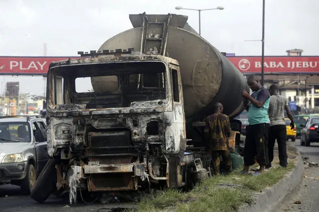 People stand next to a burnt out truck on a highway in Lagos Saturday, October 24, 2020. (Photo by Sunday Alamba/AP Photo)