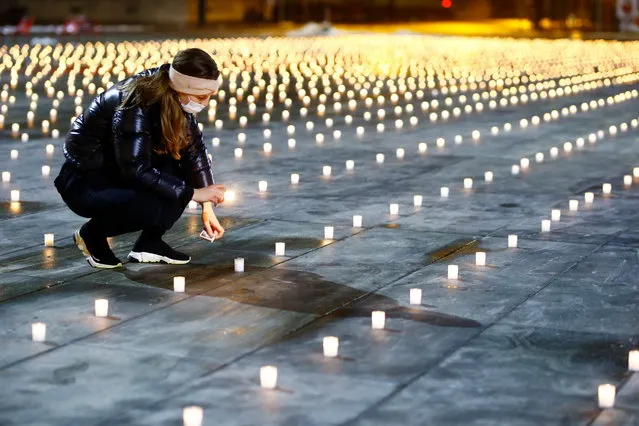 A woman lights about 5,000 candles symbolizing the coronavirus disease (COVID-19) victims during a candlelight vigil on the Bundesplatz, in front of the seat of the Swiss federal parliament, Bundeshaus, in Bern, Switzerland on December 6, 2020. (Photo by Arnd Wiegmann/Reuters)