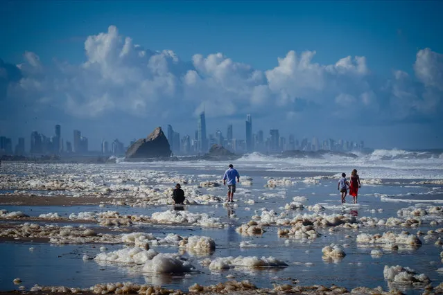 Tourists walk amongst beach foam in the wake of cyclonic conditions at Currumbin Beach on December 15, 2020, after wild weather lashed Australia's Northern New South Wales and South East Queensland with heavy rain, strong winds and king tides. (Photo by Patrick Hamilton/AFP Photo)