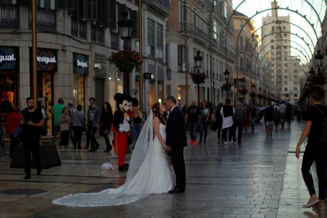 A man dressed up as Mickey Mouse watches a newly married couple posing for a wedding photographer as he performs at Marques de Larios in downtown Malaga, southern Spain, October 29, 2016. (Photo by Jon Nazca/Reuters)
