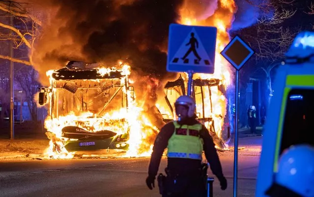 An anti-riot police officer stands next to a city bus burning in Malmo late April 16, 2022. The unrest in Malmo has continued after Rasmus Paludan, party leader of the Danish right-wing extremist party Tight Course, held a demonstration on April 16, 2022 at Skanegarden near the Oresund Bridge. (Photo by Johan Nilsson/TT News Agency/AFP Photo)
