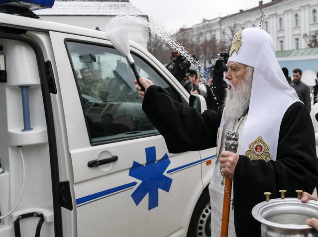 Metropolitan Filaret, the head of one of Ukraine's Orthodox churches, sprinkles holy water during a ceremony to bless ambulances, at the Mikhailovsky Zlatoverkhy Cathedral (St. Michael's Golden-Domed Cathedral) in central Kiev January 27, 2015. Three ambulances bought with donations from the faithful were blessed during the ceremony, and will be transferred to Ukrainian servicemen fighting in east Ukraine. (Photo by Gleb Garanich/Reuters)