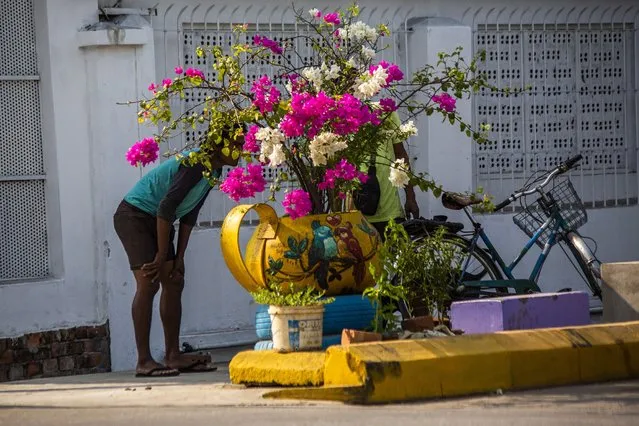 People stand behind a sidewalk flower pot watch as soldiers and police remove improvised barricades installed by anti-coup protesters and residents to secure a neighborhood from security forces in Yangon, Myanmar Thursday, March 18, 2021. (Photo by AP Photo/Stringer)