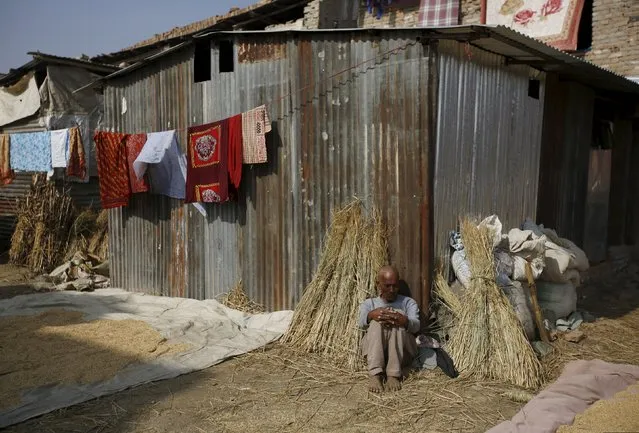 An earthquake victim sits in the sun to keep warm outside a temporary shelter built near houses damaged during an earthquake earlier this year, in Bhaktapur, Nepal November 19, 2015. (Photo by Navesh Chitrakar/Reuters)