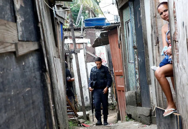 A policeman is pictured near a woman with a baby during an operation against drug dealers in Cidade de Deus or City of God slum in Rio de Janeiro, Brazil, November 23, 2016. (Photo by Ricardo Moraes/Reuters)