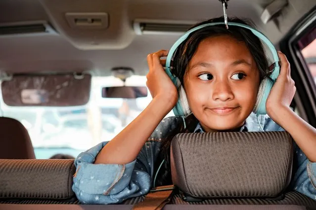 Happy and cheerful asian ethnicity teenage girl enjoy listening music through headphone on the back seat of a car. (Photo by AmpYang Images/Rex Features/Shutterstock)