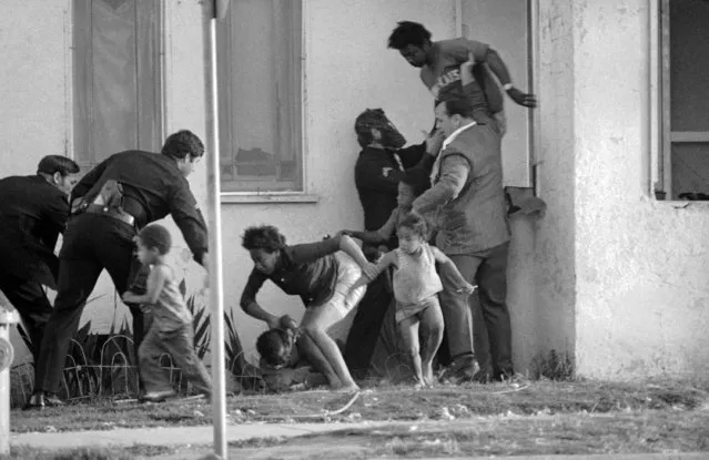 Police officers lead a group of children from a south-central Los Angeles house adjoining a suspected Symbionese Liberation Army hideout where five persons were killed in a protracted gun battle, May 17, 1974. (Photo by AP Photo)