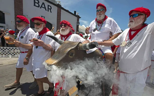 In this photo provided by the Florida Keys News Bureau, Ernest Hemingway look-alikes push a fake bull with smoke emanating from its nostrils during the “Running of the Bulls” Saturday, July 24, 2021, in Key West, Fla. A spoof of the event's namesake in Pamplona, Spain, the subtropical island city's version features fake bulls on wheels and is part of the annual Hemingway Days festival that honors author Ernest Hemingway, who lived and wrote in Key West throughout most of the 1930s. (Photo by Andy Newman/Florida Keys News Bureau via AP Photo)