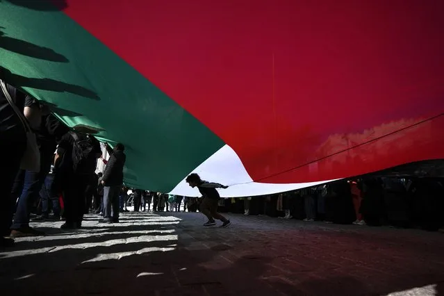 A boy passes under a giant Palestinian flag during a protest to show solidarity with the Palestinians, in Istanbul, Turkey. Friday, October 20, 2023. (Photo by Khalil Hamra/AP Photo)