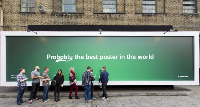 People queue by a billboard poster with a built in tap that is dispending free beer outside the Truman Brewery in east London on April 8, 2015. The 12 meter billboard poster has been created by Carlsberg as part of its “Probably the best beer in the world” campaign. (Photo by Justin Tallis/AFP Photo)