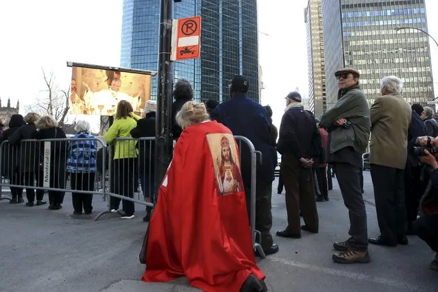 A woman prays as she watches the funeral of Cardinal Jean-Claude Turcotte broadcasted on a large screen outside of Mary, Queen of the World Cathedral in Montreal, April 17, 2015. Cardinal Turcotte died April 8, 2015 at the age of 78. (Photo by Christinne Muschi/Reuters)