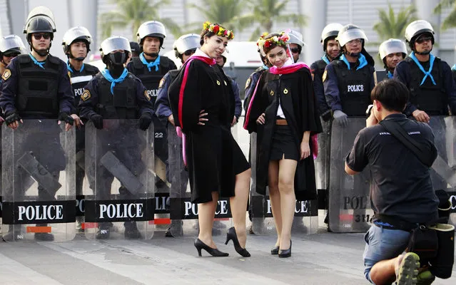 Newly graduated Thai students from Rangsit University pose for a photographer next to a group of riot policemen guarding a road near the office of the permanent secretary for defense during a rally by anti-government protesters Monday, February 3, 2014 in Bangkok, Thailand. Thai protesters vowed Monday to stage larger rallies in central Bangkok and push ahead their efforts to nullify the results of elections that were expected to prolong a national political crisis. (Photo by Wason Wanichakorn/AP Photo)