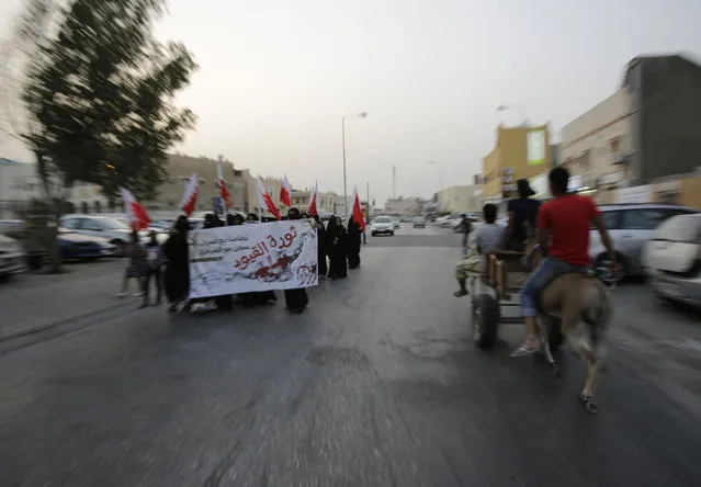 A small group of Bahraini women, carrying national flags and a banner supporting political prisoners, march quickly between police patrols, on the lookout for violators of a protest ban, in Manama, Bahrain, Friday, May 1, 2015. The government denied permission for Labor Day protests, so protesters in several opposition areas went out in small groups for quick marches between police patrols. The banner reads: “Revolution of Chains, in solidarity with Jaw central prison inmates”. (Photo by Hasan Jamali/AP Photo)