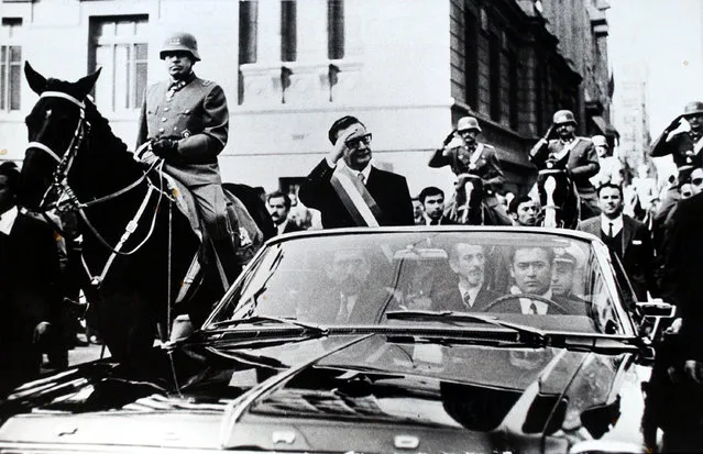 Chilean President Salvador Allende salutes from an open vehicle as General Augusto Pinochet rides on horseback at left in Santiago, Chile, May 21, 1972. (Photo by AP Photo/File)