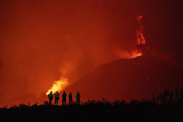 Police officers and emergency personnel look as lava flows from a volcano as it continues to erupt on the Canary island of La Palma, Spain, Tuesday, November 2, 2021. A volcano on the Spanish island of La Palma that has been erupting for six weeks has spewed more ash from its main mouth a day after producing its strongest earthquake to date. (Photo by Emilio Morenatti/AP Photo)