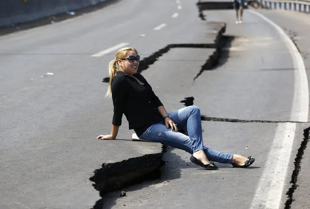 A woman poses for a picture for a friend (not pictured) while sitting on cracks on the road leading to Alto Hospicio commune, after a series of aftershocks, in the northern port of Iquique, Chile, April 3, 2014. A powerful 7.6-magnitude earthquake struck off northern Chile late on Wednesday but there were no reports of damage and a precautionary tsunami alert along the coast and in neighboring Peru was called off. (Photo by Ivan Alvarado/Reuters)