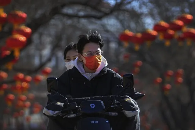 Residents wearing face masks to help protect from the coronavirus ride an electric scooter along a street decorated with red lanterns in Beijing, Tuesday, February 8, 2022. (Photo by Andy Wong/AP Photo)
