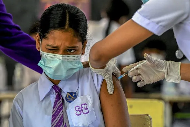 A school girl reacts as a health worker inoculates her with the dose of Pfizer-BioNTech vaccine against the Covid-19 coronavirus for the 12-15 years age group at an educational institution in Colombo on January 7, 2022. (Photo by Ishara S. Kodikara/AFP Photo)