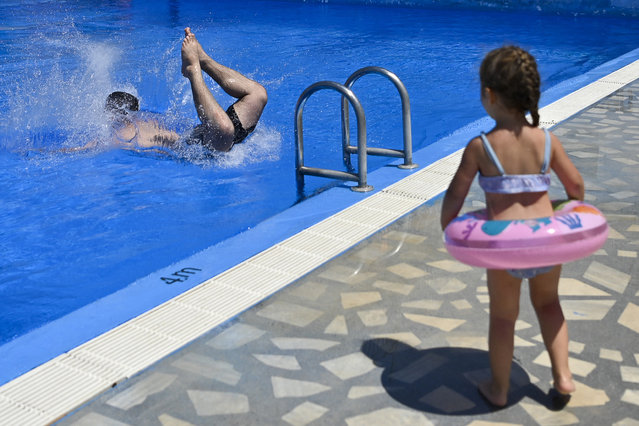 A girl watches as a man jumps to cool off at a swimming pool in the village of Zllakuqan near the town of Klina on July 9, 2024. (Photo by Armend Nimani/AFP Photo)