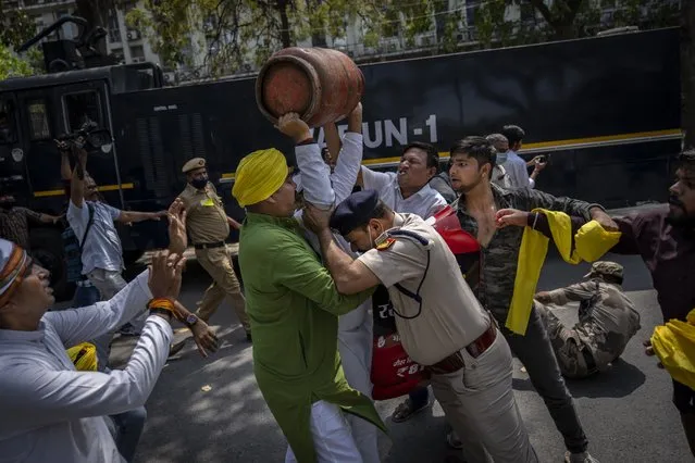 A Delhi police officer tries to stop an opposition Congress party supporter as he raises an empty Liquefied Petroleum Gas (LPG) cylinder over his head during a protest against rising inflation and price hike of essential commodities in New Delhi, India, Wednesday, March 23, 2022. (Photo by Altaf Qadri/AP Photo)