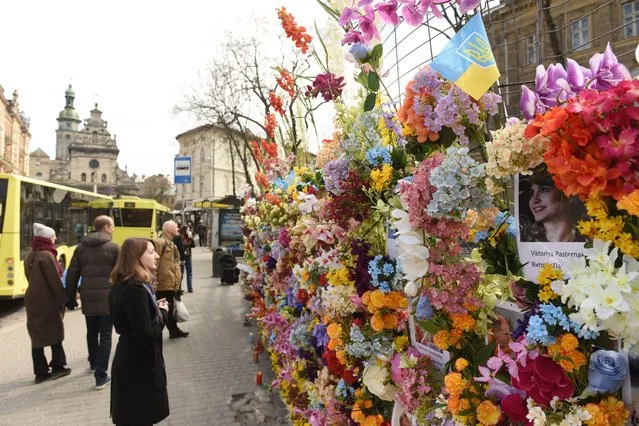 Passersby contemplate a wall of artificial flowers set up by the US-based Wall of Flowers Foundation in memory of the victims of Russia's invasion, in Ukraine's western city of Lviv on April 24, 2022. Leo Soto, who set up the foundation, says he saw how comforting a similar memorial was after a building collapse in the US state of Florida in June, and travelled to Ukraine to try to offer Ukrainians a similar level of comfort. (Photo by Yuriy Dyachyshyn/AFP Photo)