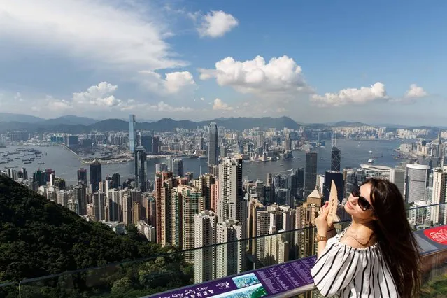 A tourist holds a traditional fan as she stands in front of a view of Hong Kong's skyline from the Peak on June 22, 2016. Hong Kong was named the world's most expensive city for expatriates, reports said on June 22 citing an annual survey. (Photo by Anthony Wallace/AFP Photo)