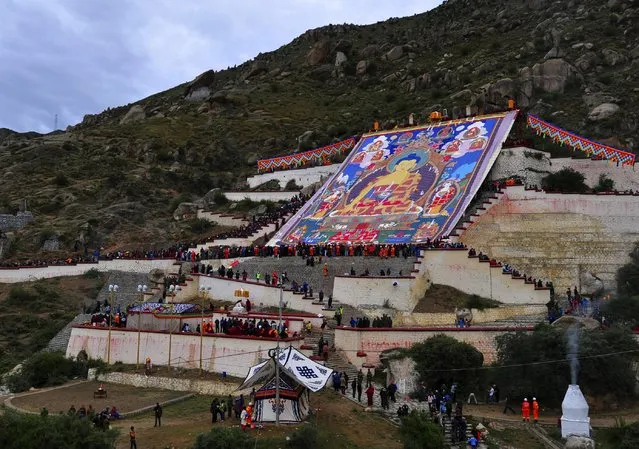Tibetan Buddhists and tourists view a huge Thangka, a religious silk embroidery or painting displaying a Buddha portrait, during the Shoton Festival at Drepung Monastery in Lhasa, Tibet Autonomous Region, China, August 14, 2015. (Photo by Reuters/China Daily)