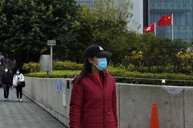 A woman wearing a face mask walks in front of flags of China, right, and Hong Kong, in Hong Kong Sunday, February 16, 2020. COVID-19 viral illness has sickened tens of thousands of people in China since December. (Photo by Vincent Yu/AP Photo)